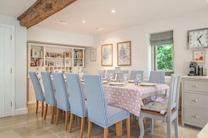 Un coin repas avec des chaises à rayures, une table recouverte d’une nappe à motifs floraux et, au mur, des reproductions encadrées de gravures botaniques.