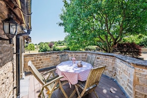 Un patio exterior con un muro de piedra, una mesa redonda con mantel estampado y sillas de madera.