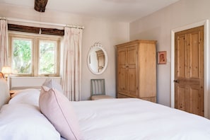 Un dormitorio con cama, armario de madera, espejo y ventana con cortinas.