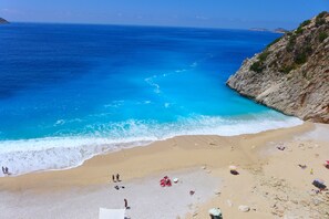 Ein Strand mit klarem, blauem Wasser, steinigen Klippen und einigen Personen.