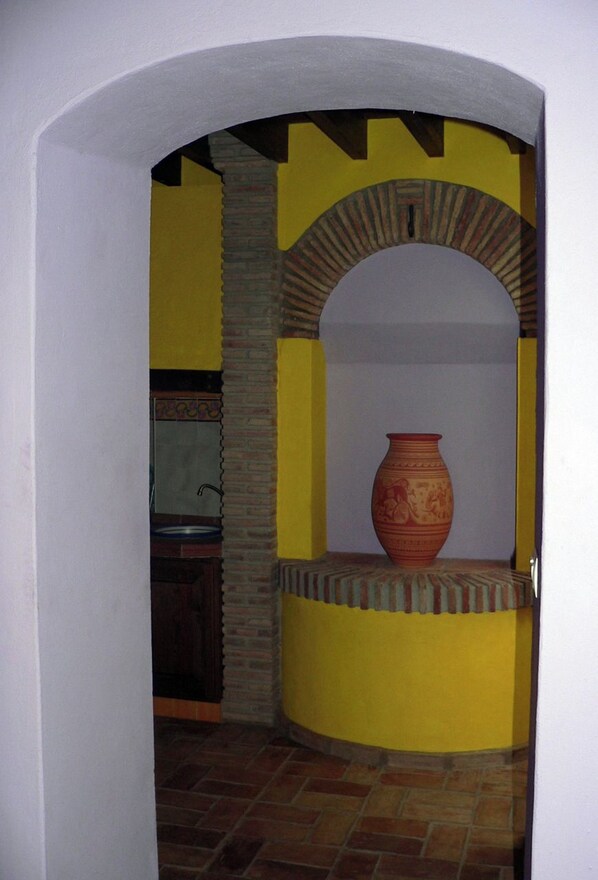 A room with a yellow wall, a large vase, and a brick fireplace.