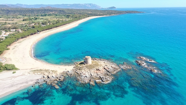 An aerial view of a coastal area with a sandy beach, clear blue waters, and a rocky island with a tower. - Sa Domu De Sa Murta 1B: 200 mtr to Baia Marina!!! Free Bikes & Kayaks. IUN P2964 (Torre di Bari)
