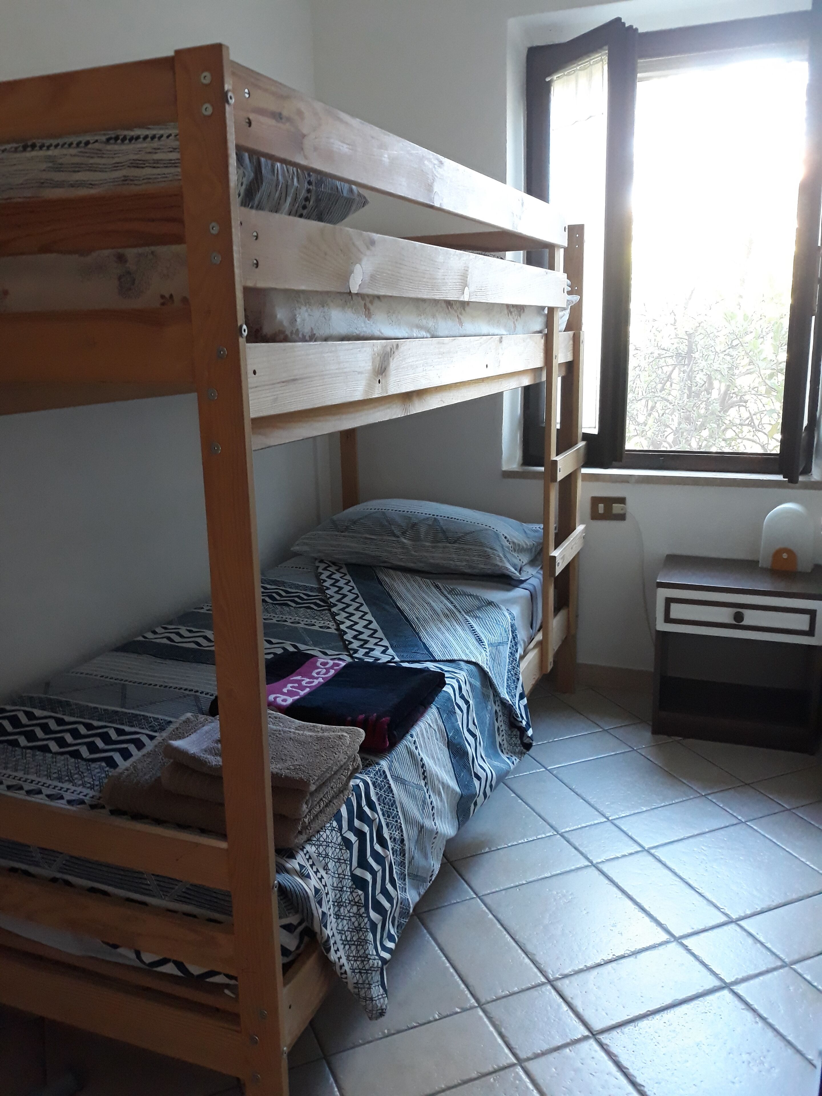 Een slaapkamer met een stapelbed, een nachtkastje en een betegelde vloer.