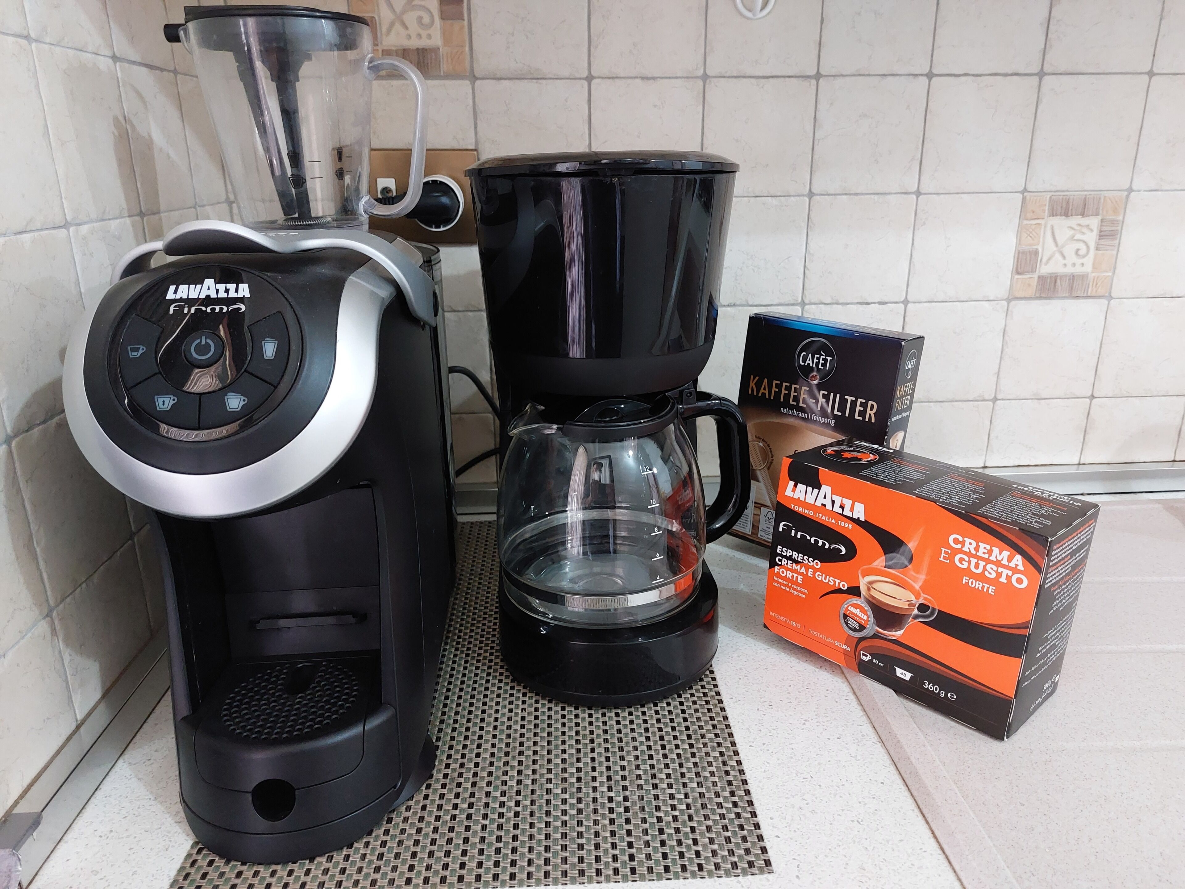A coffee maker, a coffee pot, and coffee capsules on a kitchen counter.