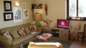 Un salón con un sofá, una mesa de centro, un televisor y una ventana que da a vista de árboles.