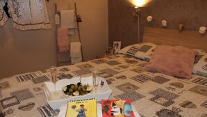 Una cama bien hecha con una colcha estampada, una mesita de noche con un vaso de agua y un frutero, y dos tarjetas decorativas sobre la cama.