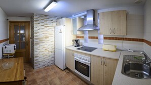 Cocina compacta con refrigerador, estufa, lavamanos y gabinetes de madera.