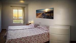 Un dormitorio con dos camas, una ventana que ofrece vistas de la ciudad y un cuadro colgado en la pared de una playa.