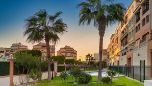 Una piscina rodeada de palmeras y un césped cuidado, con edificios residenciales al fondo.