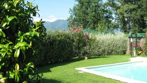 Una piscina circondata da prato curato e varie piante, con vista sulle montagne.