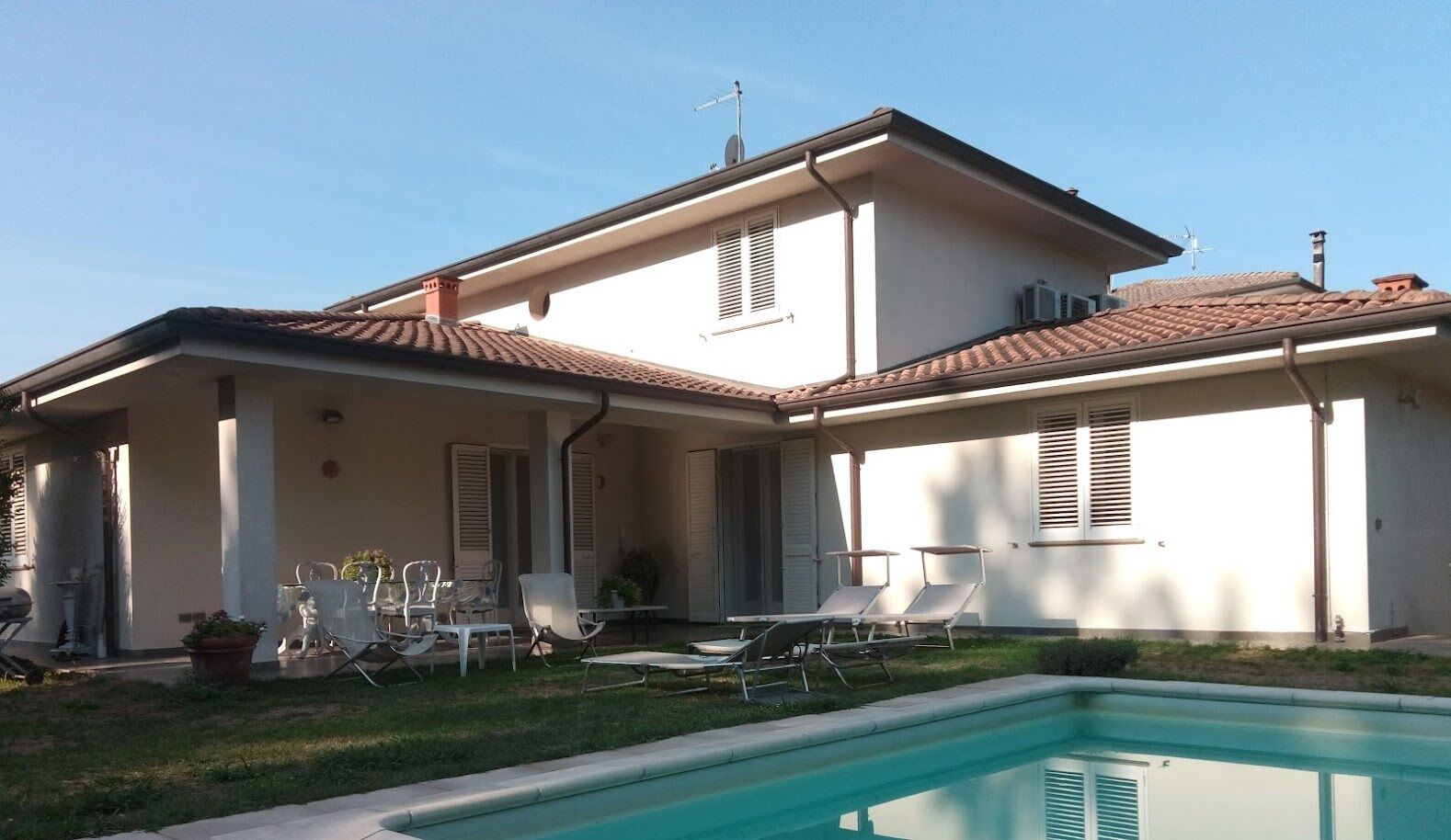 A two-story house with a swimming pool, outdoor seating, and a clear sky.