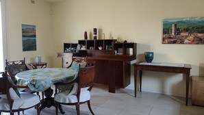 Un'area pranzo con tavolo e sedie in legno, un armadietto con ripiani e un quadro appeso al muro.