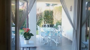 Vista attraverso una porta su un patio esterno con tavolo e sedie, una pianta in vaso e pavimento piastrellato.