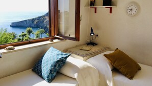 Une pièce confortable avec vue sur la mer, une fenêtre avec un cadre en bois, un bureau avec une lampe et une horloge au mur.