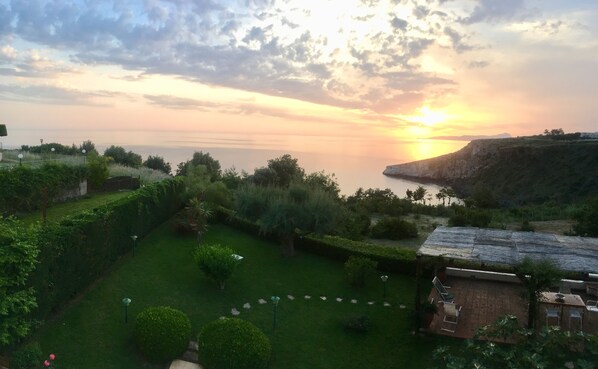 Un jardin avec un espace patio, une vue sur la mer et un coucher de soleil.