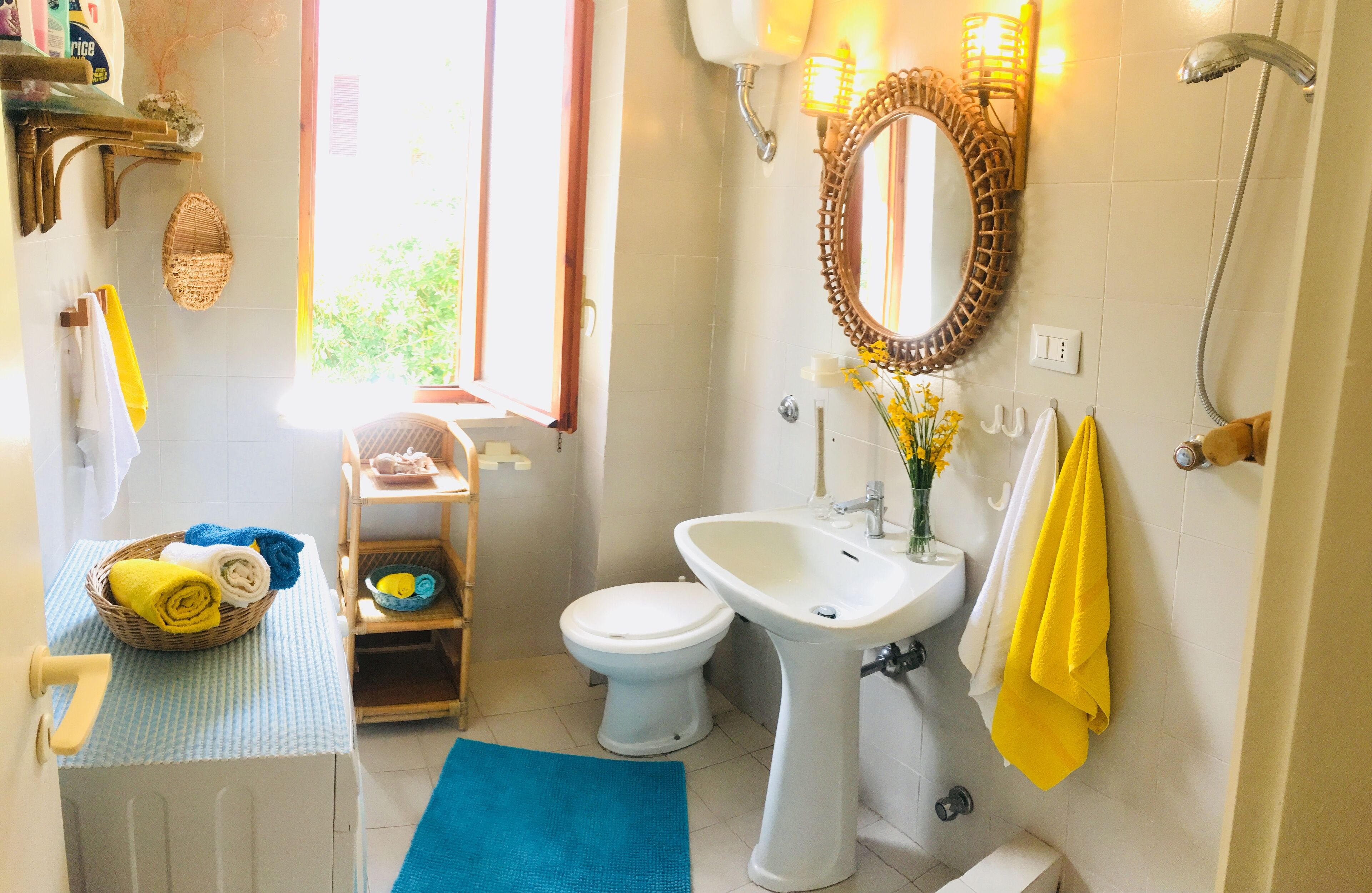 A bathroom with a white sink, a mirror, and a toilet. There is a basket of towels and a blue mat on the floor.