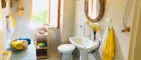 A bathroom with a white sink, a mirror, and a toilet. There is a basket of towels and a blue mat on the floor.
