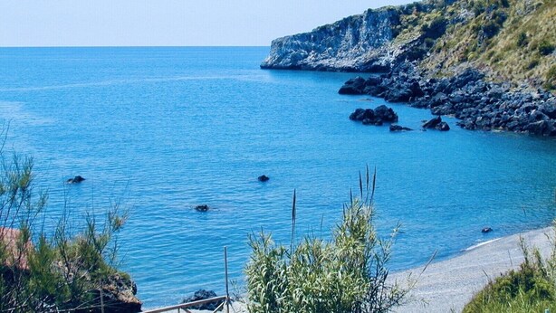 Un paysage côtier avec une eau d’un bleu limpide, des falaises rocheuses et une végétation clairsemée.