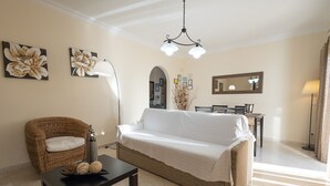 A living room with a sofa, a wicker chair, a dining table, and a lamp. - Casa Mateus (Alvor)