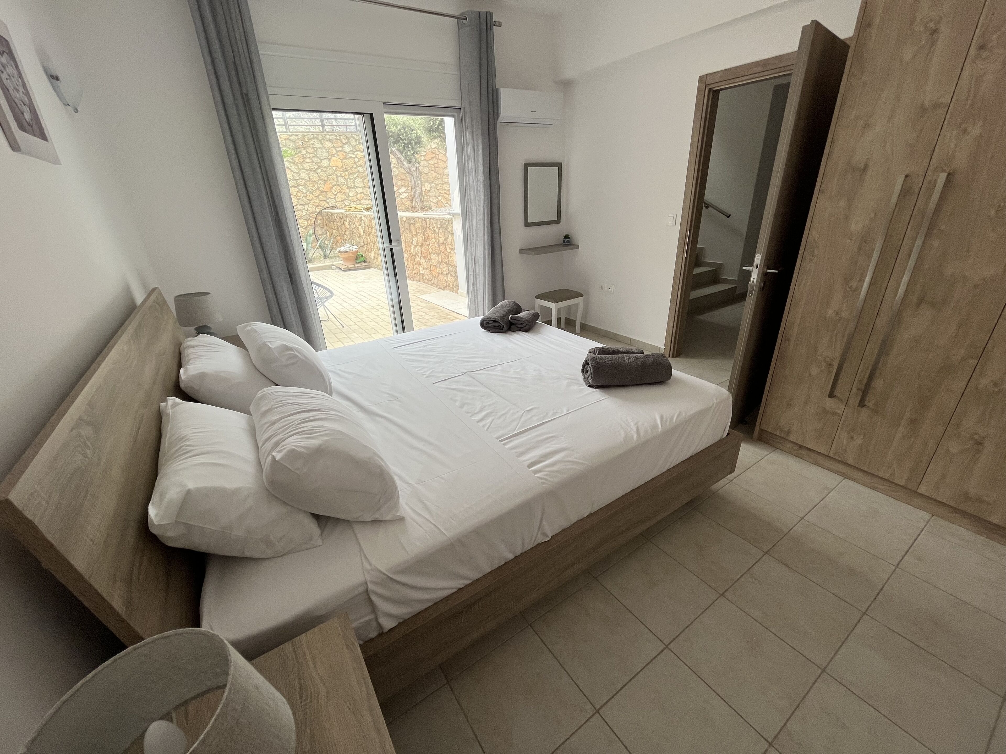 Ein Schlafzimmer mit einem großen Bett, einem Holzkopfstück, einem kleinen Nachttisch, einem Spiegel und einem Kleiderschrank.