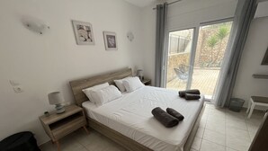 A neatly made bed with white linens and rolled towels, a bedside table with a lamp, and a small plant. - Beautiful villa with private pool & garden and stunning views of Navarone Bay. (Lindos)