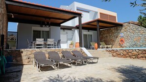 A modern house with a covered patio, stone wall, and a pool area with lounge chairs. - Beautiful villa with private pool & garden and stunning views of Navarone Bay. (Lindos)