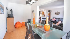 Ett modernt vardagsrum med ett matbord i glas, orange sittpuffar, en soffa och en dekorativ orange vas.