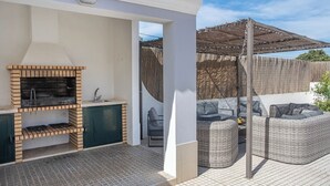 En uteplats med en grillmur av tegel, möbler av rotting och en överbyggd sittplats.