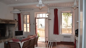 A cozy room with a fireplace, a television, a dining table, and a window with red curtains. - charming fisherman house (Gruissan)