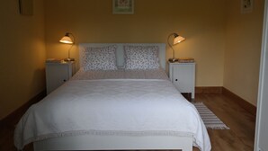 A neatly made bed with a floral headboard, two bedside tables with lamps, and a framed picture on the wall. - Cosy, rustic, holiday home, near the coast and mountains, (Asturias)