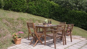 A wooden table with four chairs, a basket, and two bottles on a paved patio. - Cosy, rustic, holiday home, near the coast and mountains, (Asturias)