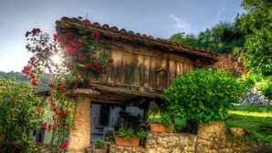 A rustic stone building with a wooden facade, surrounded by lush greenery and flowering plants. - Cosy, rustic, holiday home, near the coast and mountains, (Asturias)