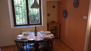 A dining area with a round table set for four, a bottle of wine, and a window with a view of trees. - Cosy, rustic, holiday home, near the coast and mountains, (Asturias)