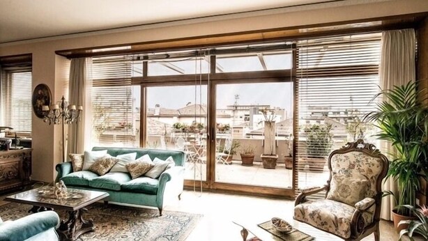 A spacious living room with a large sliding glass door leading to a balcony, a green sofa, a patterned armchair, and a coffee table. - The best choice for your vacation in Venice! (Venezia)