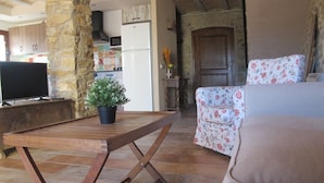 Een gezellige zithoek met een stenen muur, een houten tafel, een potplant, een bloemenbank en een televisie.