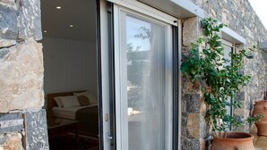 A room with a bed, a sliding glass door, stone walls, and potted plants.