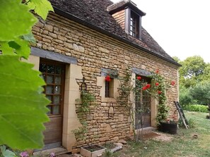 Traditional stone building with a pitched roof and dormer window, surrounded by a charming garden with flowering plants.