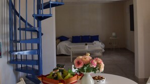 A room with a white round table, a blue spiral staircase, a bed with blue pillows, and a small white table with a vase of flowers. - Vendicari time, just steps away from the calamus beaches and vendors (NOTO)