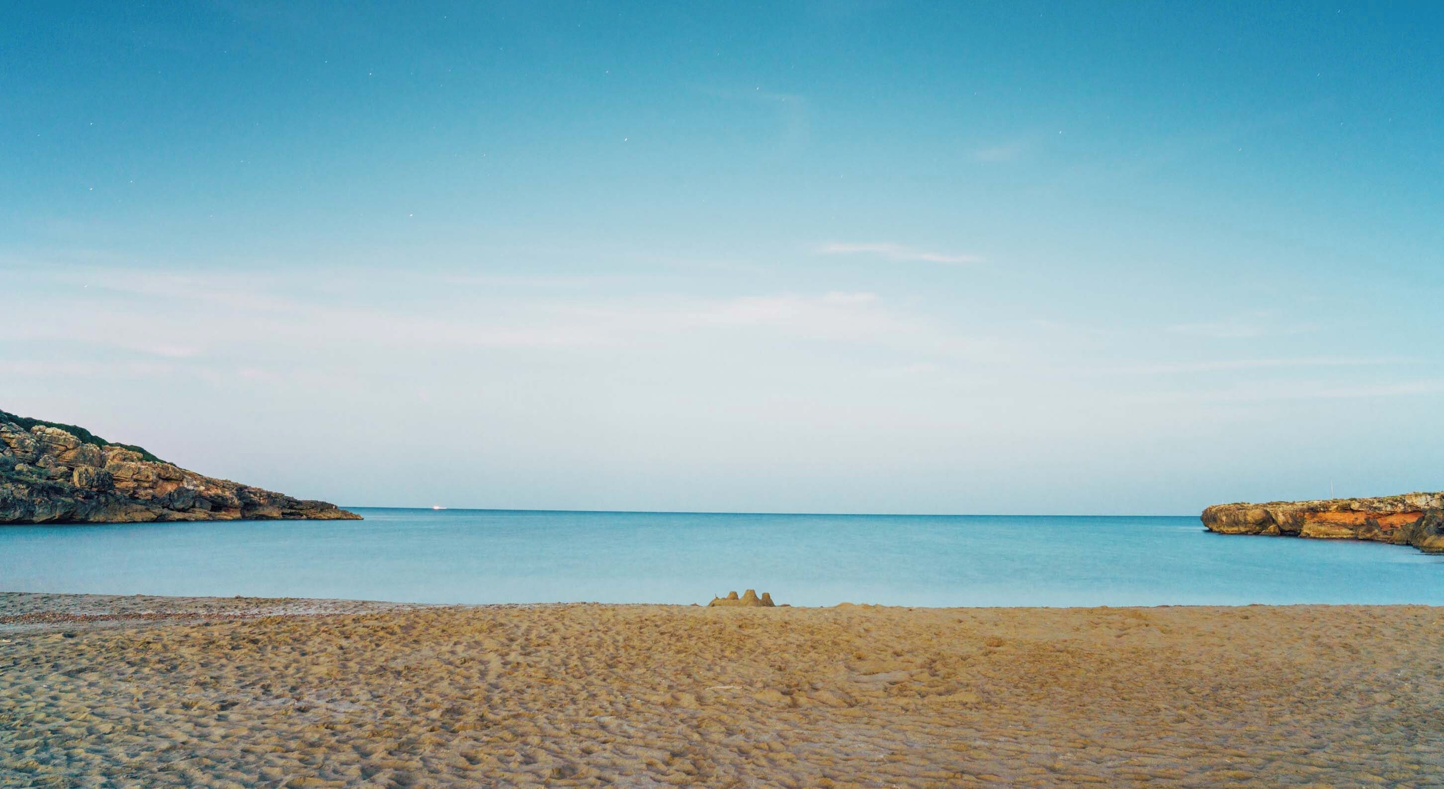 Une plage avec une eau d’un bleu limpide et des formations rocheuses.