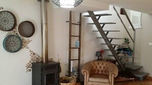 A living room with a fireplace, a ladder, a chair, and a staircase.