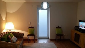 A living room with a sofa, two chairs, a television, and a door.
