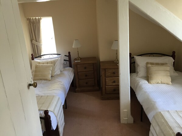 A bedroom with two single beds, a nightstand with a lamp, a wooden dresser, and a window with curtains. - Lovely Character Dartmoor Cottage Just Below the Famous Haytor Rocks (Newton Abbot)