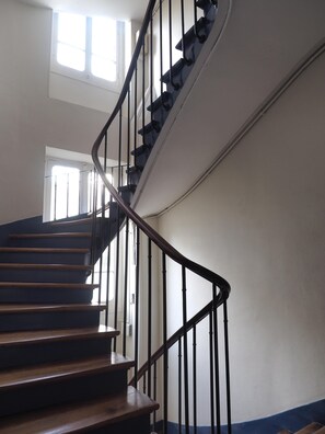 A spiral staircase with wooden steps and black metal railings, leading to an upper floor. - Charm and garden view, in the center of Paris, near Montparnasse (Paris)