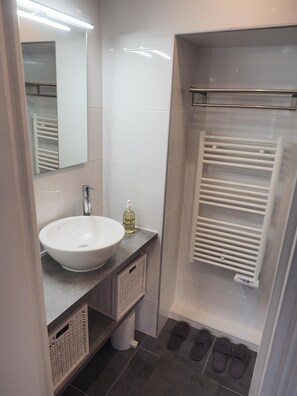 A modern bathroom with a white sink, a mirror, a towel rack, and a shower area. - Charm and garden view, in the center of Paris, near Montparnasse (Paris)