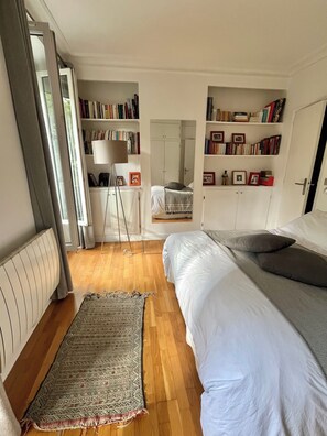 A bedroom with a bed, a bedside table, a floor lamp, a bookshelf, and a wardrobe.