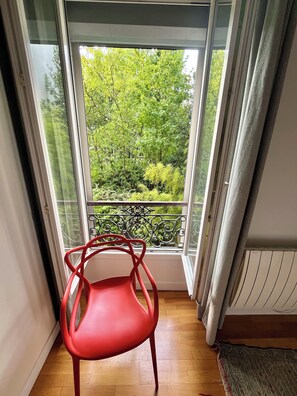 A red chair in a room with a view of a balcony, a radiator, and a patterned rug.