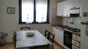 A kitchen with a dining table, chairs, a window with curtains, cabinets, a stove, and a fire extinguisher. - Apartment 2 km from the sea, 200 meters from the historic center of bosa (Bosa, Oristano)