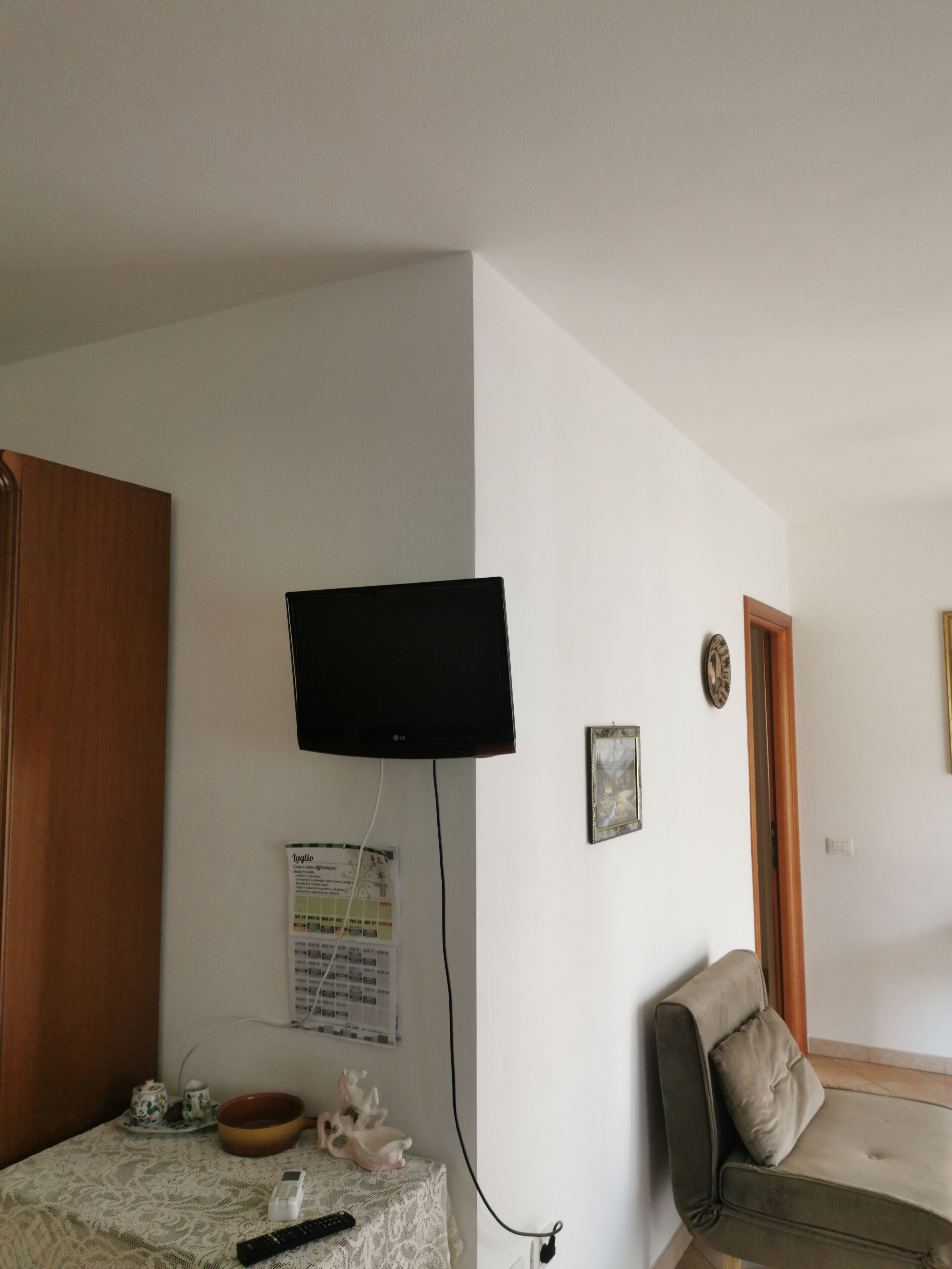 Ein Zimmer mit an der Wand montiertem Fernseher, einer Couch, einem kleinen Tisch mit Schale und Figur sowie einer Tür.
