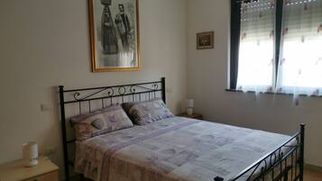 Una camera da letto con un letto, un comodino, una cassettiera, un quadro appeso al muro e una finestra con tende.