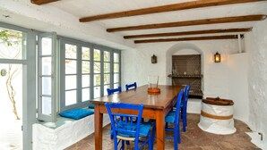 Un coin repas avec une table en bois, des chaises bleues et un banc agrémenté de coussins.